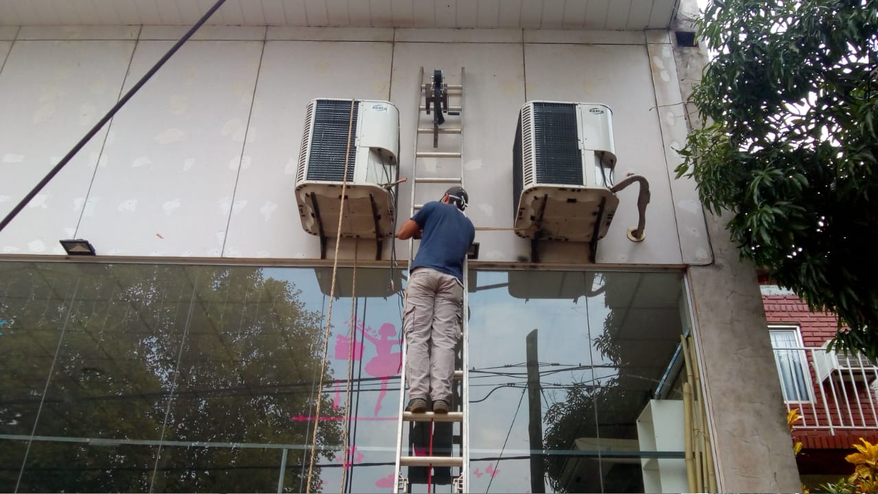 Tecnico usando una escalera para reparar un aire acondicionado